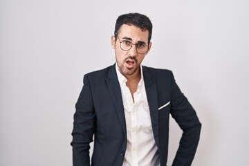 Handsome business hispanic man standing over white background in shock face, looking skeptical and sarcastic, surprised with open mouth