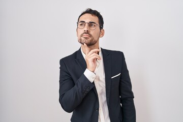 Handsome business hispanic man standing over white background thinking concentrated about doubt...