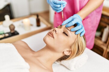 Naklejka premium Young caucasian woman lying on table having antiaging treatment at beauty salon