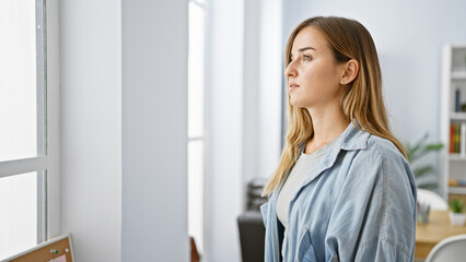 Serious-faced young blonde business woman, intently looking through the office window, displaying her concentration at work