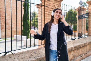 Fototapeta premium Young beautiful hispanic woman listening to music and dancing at street