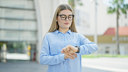 Young blonde woman business worker looking watch with serious expression at street
