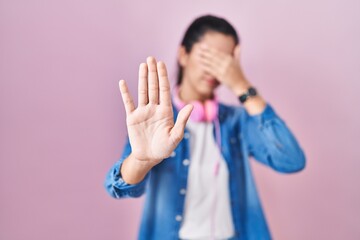 Young beautiful woman standing over pink background covering eyes with hands and doing stop gesture with sad and fear expression. embarrassed and negative concept. - obrazy, fototapety, plakaty