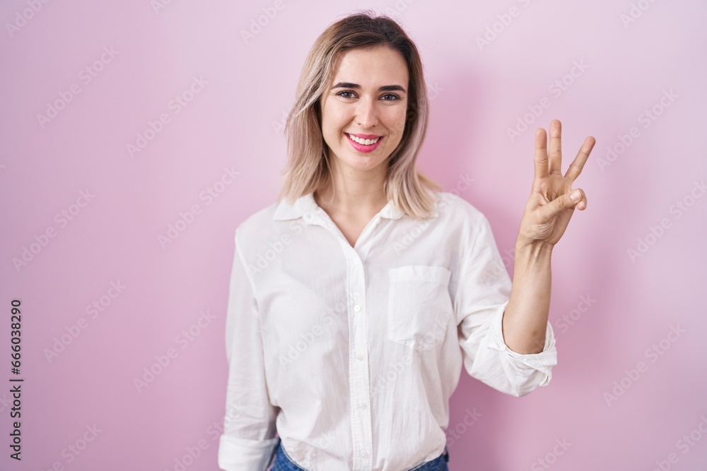 Canvas Prints Young beautiful woman standing over pink background showing and pointing up with fingers number three while smiling confident and happy.