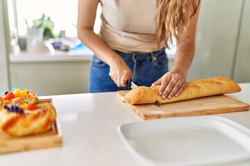 Young beautiful hispanic woman preparing breakfast cutting bread at the kitchen