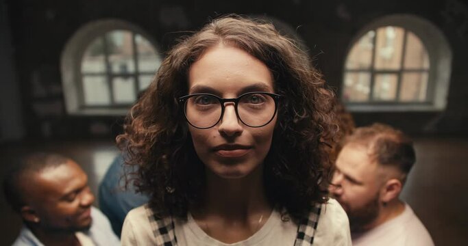 Portrait of a brunette girl with curly hair in glasses who looks at the camera and then falls into the arms of her friends during group therapy and trust practice