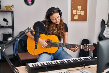 Young beautiful hispanic woman musician playing classical guitar at music studio