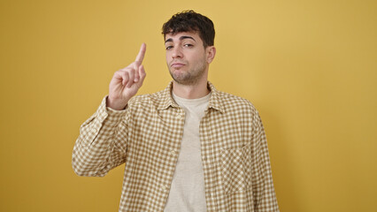 Young hispanic man saying no with finger over isolated yellow background