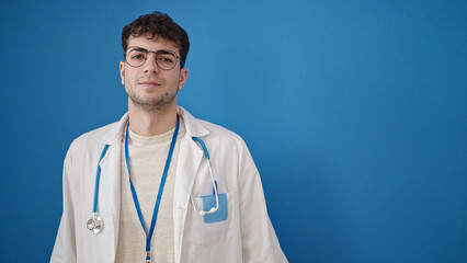 Young hispanic man doctor standing with serious expression over isolated blue background