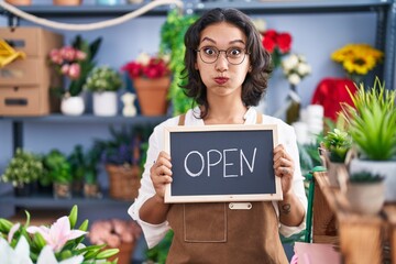 Young hispanic woman working at florist holding open sign puffing cheeks with funny face. mouth inflated with air, catching air. - obrazy, fototapety, plakaty