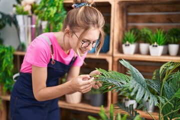 Obraz premium Young blonde woman florist smiling confident touching plant at flower shop