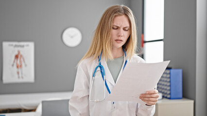 Young blonde woman doctor reading document at clinic