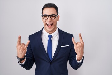 Young hispanic man wearing suit and tie shouting with crazy expression doing rock symbol with hands...