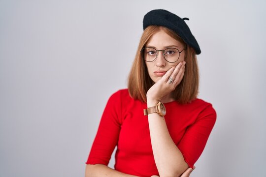 Young redhead woman standing wearing glasses and beret thinking looking tired and bored with depression problems with crossed arms.