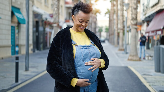 Young pregnant woman smiling confident touching belly at street