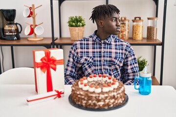 African man with dreadlocks celebrating birthday holding big chocolate cake looking to side, relax profile pose with natural face with confident smile.