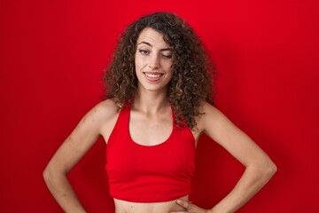 Hispanic woman with curly hair standing over red background winking looking at the camera with sexy...