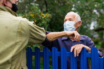 Senior man in mask having conversation with his neighbour