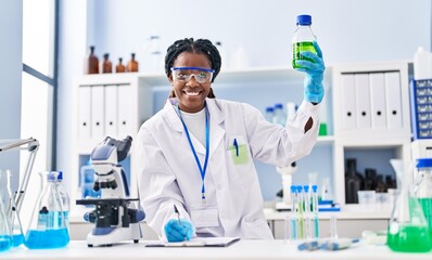 Fototapeta premium African american woman scientist holding bottle writing on document at laboratory
