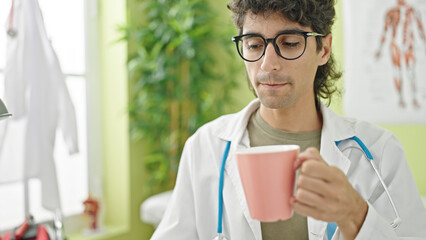 Young hispanic man doctor drinking coffee at clinic