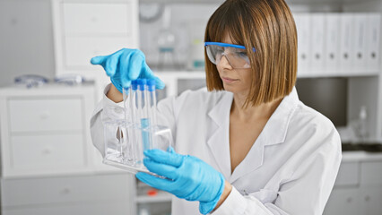 Young beautiful hispanic woman scientist looking at test tubes at laboratory