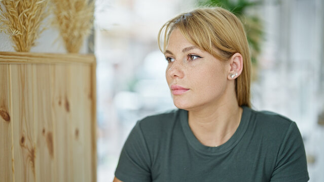 Young blonde woman sitting on table looking to the side at coffee shop