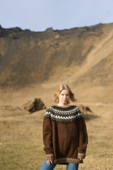 A girl in fashion clothes poses in mountains an Icelandic sweater