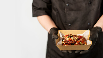 The cook holds in his hands a box with grilled spicy chicken