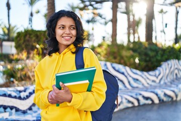 Young latin woman student smiling confident holding books at park
