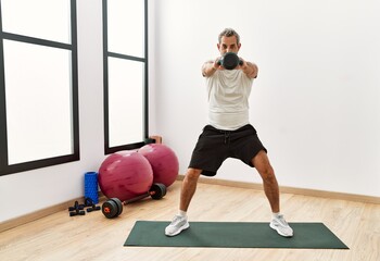 Middle age grey-haired man using kettlebell training at sport center