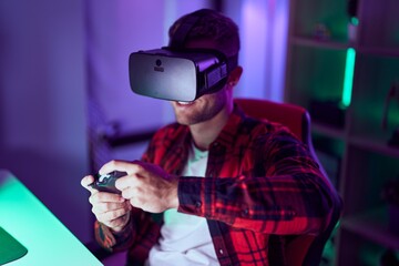 Young caucasian man streamer playing video game using virtual reality glasses and joystick at gaming room