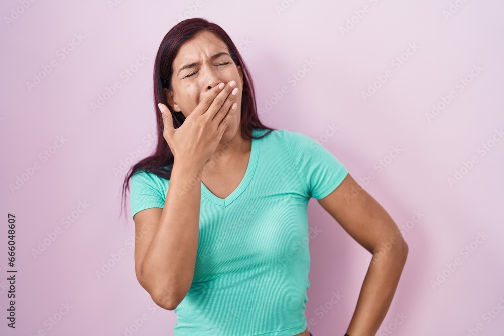 Sticker young hispanic woman standing over pink background bored yawning tired covering mouth with hand. res