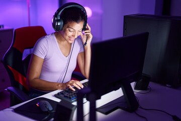 Young beautiful hispanic woman streamer playing video game using computer at gaming room