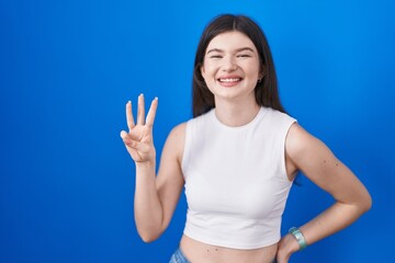 Fototapeta na wymiar Young caucasian woman standing over blue background showing and pointing up with fingers number three while smiling confident and happy.