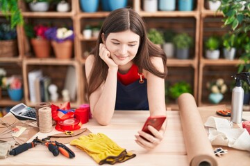 Young caucasian woman florist smiling confident using smartphone at florist