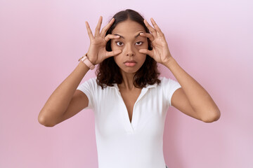 Young hispanic woman wearing casual white t shirt trying to open eyes with fingers, sleepy and...