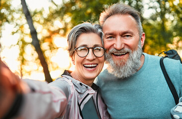 Wonderful sincere cheerful couple of gray haired mature smiling people taking selfie portrait on phone. Today's active retirees are enjoying life. A man with a gray beard and a woman in glasses. - obrazy, fototapety, plakaty