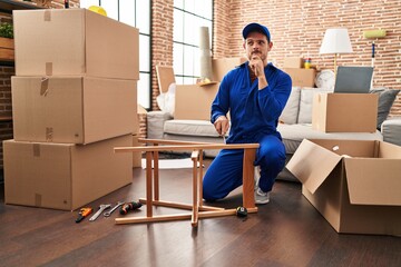 Young hispanic man working on moving service serious face thinking about question with hand on...