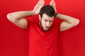 Fototapeta na wymiar Young hispanic man wearing casual red t shirt doing bunny ears gesture with hands palms looking cynical and skeptical. easter rabbit concept.