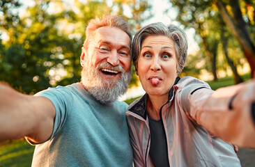 Positive, cheerful, smiling gray-haired couple of senior people make a photo while grimacing. The man laughs, the woman shows her tongue funny. Senior people are emotionally happy and enjoying life.