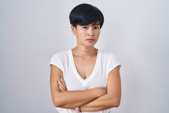 Young asian woman with short hair standing over isolated background skeptic and nervous, disapproving expression on face with crossed arms. negative person.