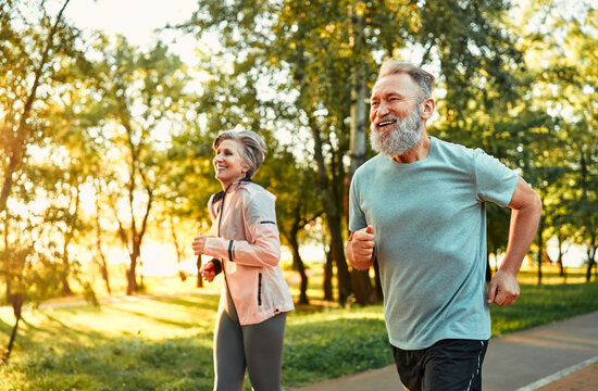 Senior family couple jogging. Mature fitness people feeling contentment when running together in park. Cheerful loving spouses standing for healthy lifestyle and training every day outdoors.