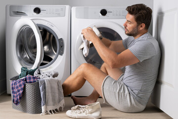 Portrait of sexy man with dirty clothes near washing machine. Handsome man sits in front of washing...