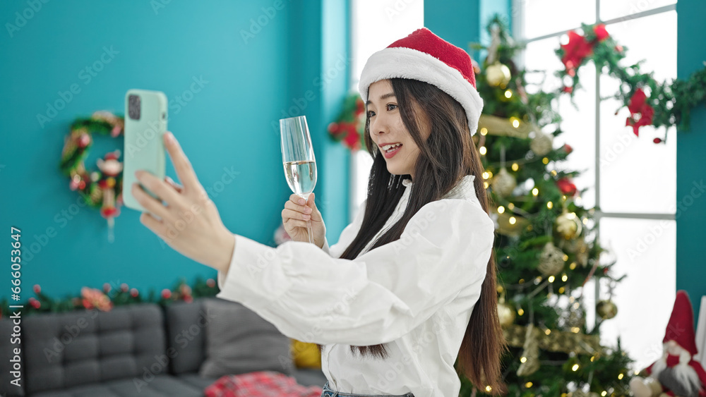 Poster Young chinese woman celebrating christmas holding glass of champagne having video call at home