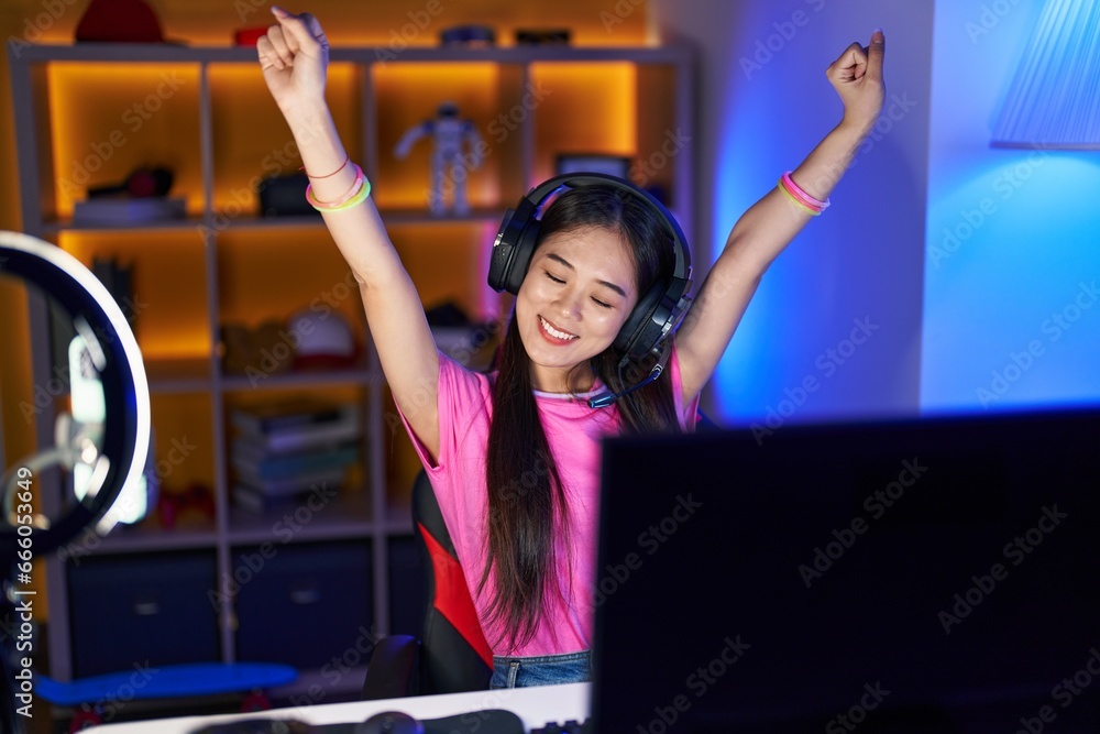 Sticker Young chinese woman streamer playing video game with winner expression at gaming room