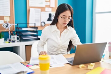 Young chinese woman business worker using laptop reading document at office