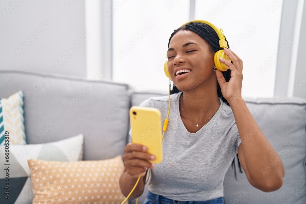 Wall mural African american woman listening to music sitting on sofa at home