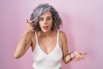 Middle age woman with grey hair standing over pink background confused and annoyed with open palm...