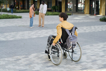 Rear view of young man with disability moving in wheelchair in the city