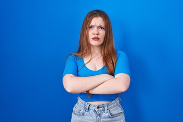 Redhead woman standing over blue background skeptic and nervous, disapproving expression on face...